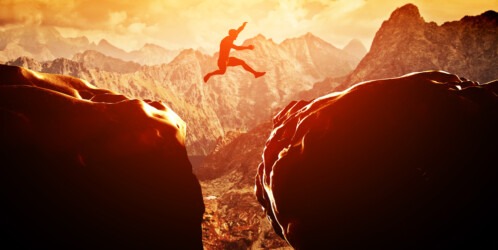Man,jumping,over,precipice,between,two,rocky,mountains,at,sunset.
